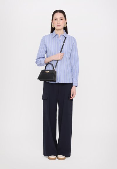 Striped blue button-up shirt, dark wide-leg pants, and a black structured handbag. Footwear is light-colored with a flat sole.