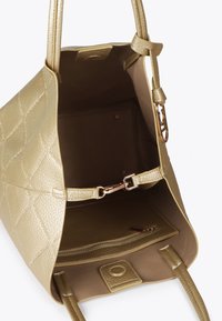 Złota torebka pikowana z otwartym wierzchem, ukazująca przestronne wnętrze i zapinaną na zamek przegródkę w środku.