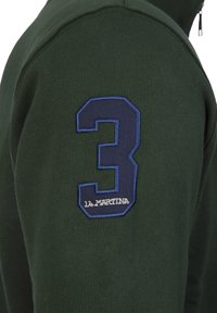 Green sweatshirt featuring a blue embroidered number 3 and “LA MARTINA” logo on the left sleeve, with a smooth texture and fitted design.