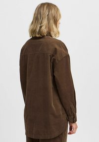 Camisa de pana marrón con un corte relajado, mangas largas y dobladillo curvado. La espalda presenta un detalle en yugo y puños de manga abotonados.