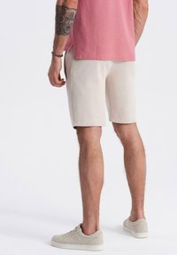 Shorts beiges en tissu doux avec une taille élastique, associés à une chemise rose et des baskets gris clair. Présente un design minimal et une coupe simple.