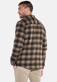 Brown and black plaid flannel shirt with long sleeves, a relaxed fit, and a straight back hem. Features pocket openings at the sides.