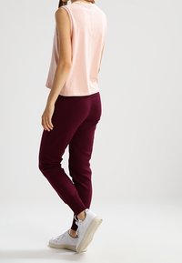 Mouwloos lichtroze topje gecombineerd met donkerburgundy joggerbroeken en witte sneakers. Soepele stof, ontspannen pasvorm, cropped ontwerp, minimale stikdetails.