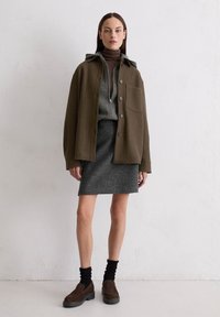 Brązowa wełniana oversizowa kurtka, szary zamek błyskawiczny sweter, szara spódnica, brązowe zamszowe buty na suwak, czarne prążkowane skarpetki, minimalny design, neutralne odcienie.