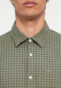 Groen geruit kortemouwenshirt van katoen. Heeft een button-down kraag en een klein geborduurd krokodil-logo op de borst.