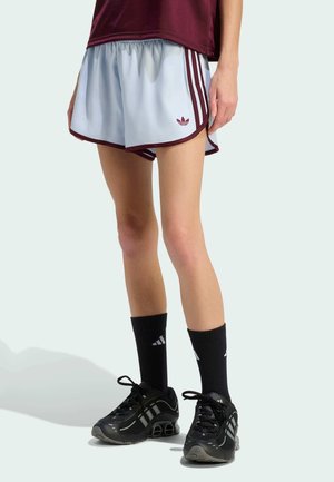 Osoba nosząca jasnoniebieskie spodenki sportowe z bordowymi paskami, czarne skarpety marki Adidas sięgające do połowy łydki oraz czarne buty do biegania na jednolitym tle.