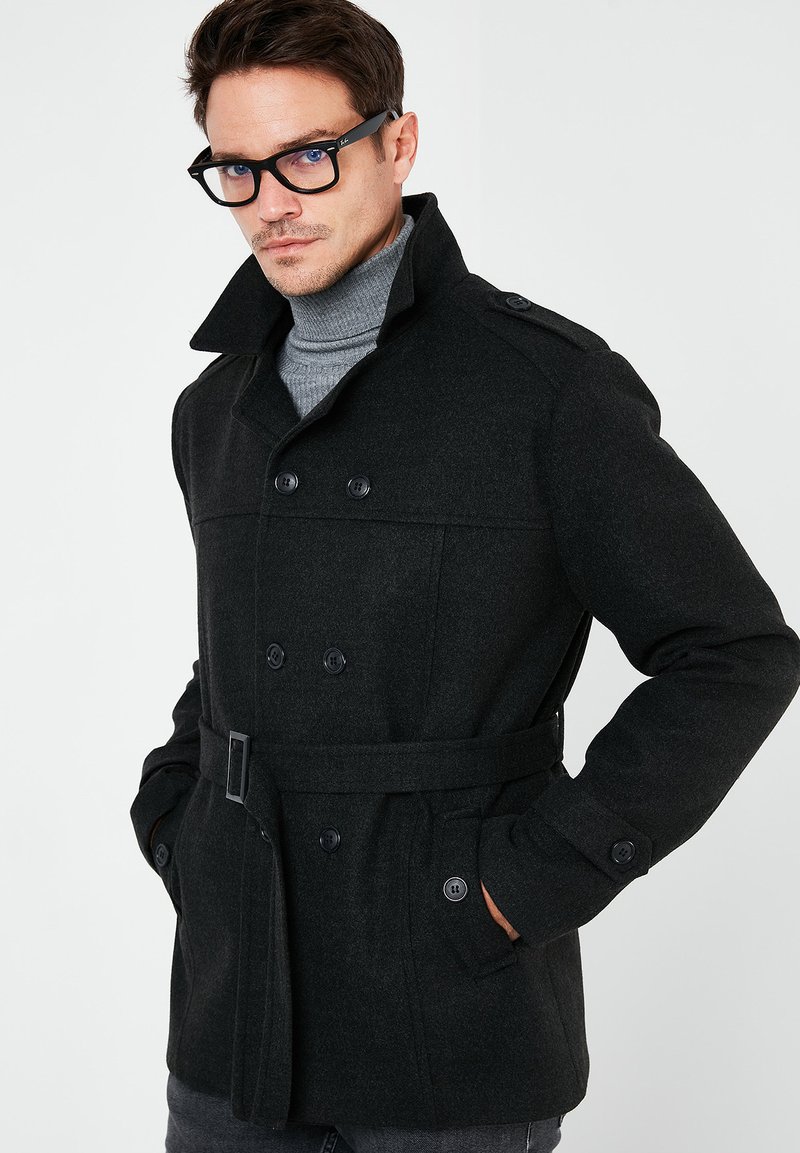 Cappotto in misto lana nero con bottoni doppi, ampio rever, vita con cintura e tasche laterali. Presenta una superficie textured.