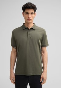 Dunkelgrünes Poloshirt aus weichem Material mit kurzen Ärmeln, drei Knöpfen und einem dezent gerippten Kragen. Sauberes, minimalistisches Design.