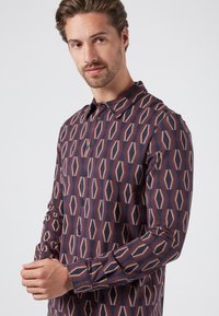 Camisa de manga larga con un patrón geométrico en colores navy, crema y óxido, con cuello y puños abotonados, y una textura suave.