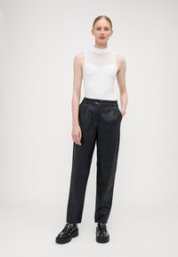 Top blanc sans manches avec un panneau en maille texturé, associé à un pantalon en cuir noir taille haute. Chaussures compensées noires avec des accents en clous.