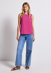 Fuksia sleeveless toppi, jossa on kerätty pääntie, yhdistettynä vaaleansinisiin leveälahkeisiin farkkuihin ja ruskeisiin liukuvaan sandaaleihin. Yksinkertainen muotoilu, jossa on sileä pinta.