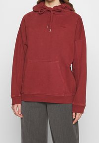 Felpa rossa in cotone con cappuccio, tasca frontale, cordino al collo e polsini e orlo a coste. Design semplice e dal taglio rilassato.