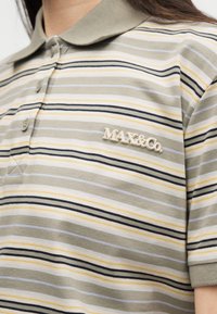 Κοντινό πλάνο μπεζ ριγωτού πόλο με κοντά μανίκια και λογότυπο MAX&Co. στο στήθος.