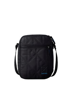 Zwarte doorgestikte crossbodytas met een ritsvak aan de voorkant, verstelbare band en een klein blauw Calvin Klein-logo patch rechtsonder.