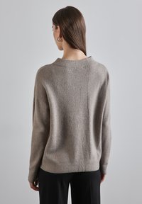 Hellbrauner Pullover mit gerippter Textur, lässiger Passform, Rundhalsausschnitt und kontrastierendem Strickdesign auf der Rückseite. Lange Ärmel und weiches Material.