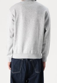 Pull gris avec col et poignets côtelés, présentant un tissu doux et texturé. Associé à un pantalon en denim foncé avec poches arrière.