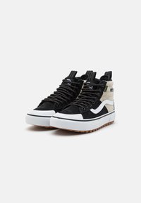 Sorte og kremfargede høyde sneakers i semsket skinn og lerret, med en hvit mellomsåle og strukturert gummisåle. Snøring er synlig.