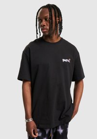 Tricou negru din bumbac, cu o croială lejeră, având un mic logo Puma alb și violet pe pieptul stâng. Mâneci scurte și guler rotund.