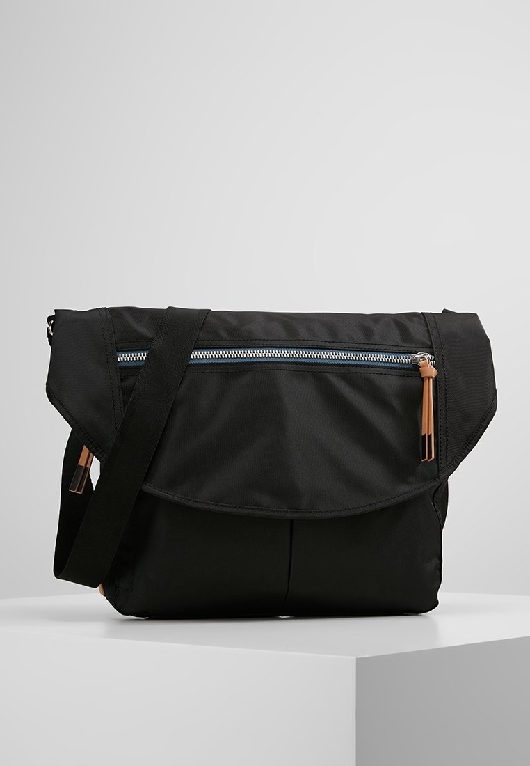 Borsa a tracolla nera realizzata in tessuto resistente, con una pattella pieghevole, tasca con zip, tracolla regolabile e dettagli in hardware beige.