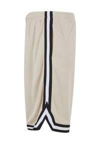 Shorts de basketball en maille beige avec des bandes latérales noires et blanches et une coupe en V à l'ourlet inférieur.