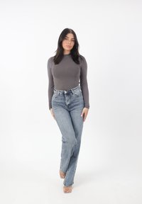 Camiseta gris de manga larga combinada con unos vaqueros de cintura alta de color azul claro. Los vaqueros tienen un corte recto y cinco bolsillos, con costuras visibles.
