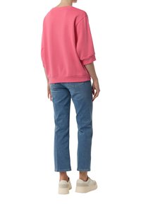 Różowa bluza z szerokimi rękawami i ściągaczami, w połączeniu z niebieskimi dżinsami. Modelka ma na sobie beżowe sneakersy na platformie.