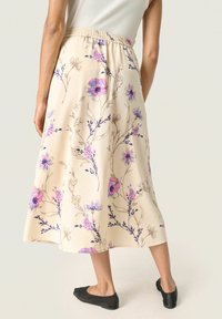 Ljusbeige blommig kjol med lila och blå blommor; har resårmidja och en mjuk silhuett, tillsammans med enkla svarta ballerinaskor.