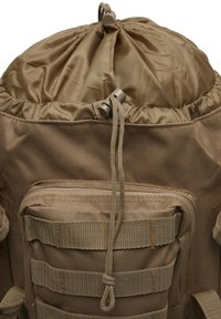 Sac à dos tactique beige avec fermeture à cordon, poche avant zippée et sangles MOLLE pour attacher du matériel ou des accessoires.