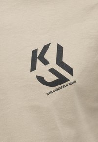 Bežna bombažna majica z črnimi logotipnimi stiliziranimi inicialkami "KL" in besedilom "KARL LAGERFELD JEANS" na dnu.