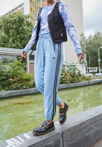 Light blue sweatpants with black stripes, a floral patterned long-sleeve shirt, and a black vest, paired with black buckle shoes.