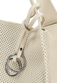 Perforowana torebka ze skórki kremowej o gładkiej fakturze, z podwójnym pierścieniem jako akcentem i wiązanym paskiem zapewniającym bezpieczne zamknięcie.