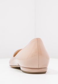 Lesklá béžová dámská plochá obuv zobrazená zezadu, zdůrazňující hladký povrch, mírný podpatek a vertikální švy na části paty.