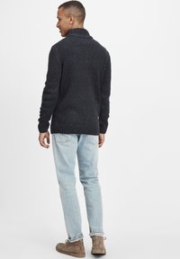 Mörk marinblå tröja med en grov stickad struktur och hög krage, kombinerad med ljusblå jeans och bruna snörkängor.