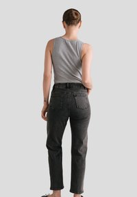Szary top na ramiączkach z okrągłym dekoltem, zestawiony z czarnymi, wysokim stanem jeansami z tylnymi kieszeniami. Gładka tkanina i dopasowany krój.
