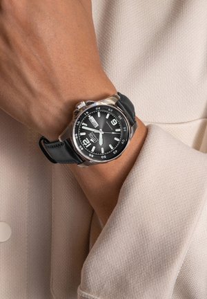 Montre analogique avec un cadran noir, un boîtier en acier inoxydable argenté et un bracelet en silicone noir. Présente de grands index horaires blancs et un affichage de la date.