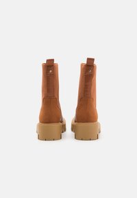 Botas de tobillo de ante marrón con paneles laterales elásticos y punteras redondeadas, que cuentan con una suela de goma beige gruesa y lengüetas en la parte trasera.