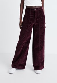 Corduroy wijdbenige broeken in diep bordeauxrood met een gestructureerde afwerking, voorzien van voorzakken en een knoopsluiting aan de taille.