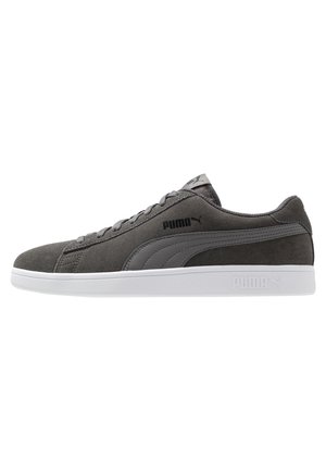 Niski szary zamszowy sneaker Puma z zapięciem na sznurówki, kontrastowym szarym paskiem i białą gumową podeszwą.