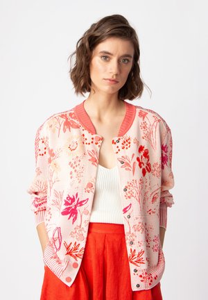 Pink floral-patterned cardigan with ribbed cuffs and collar, featuring decorative buttons and a relaxed fit, worn over a white top.