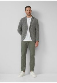 Grijze textuur blazer met een enkele knoop, gecombineerd met een wit t-shirt en groene broek. Witte sneakers maken de outfit compleet.