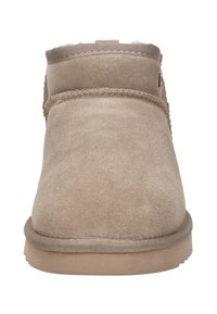 Beige suède enkellaarsjes met een ronde neus, zachte textuur, gestikte details en een platte rubberen zool. Geen zichtbare hardware of accenten.