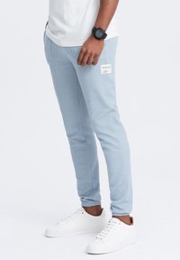 Vaaleansiniset jogginghousut, jotka on valmistettu teksturoidusta kankaasta. Niissä on sivutasku, jossa on etiketti. Yhdistettynä valkoisiin tenniskenkiin. Muotoiltu fit ja käänteet nilkoissa.