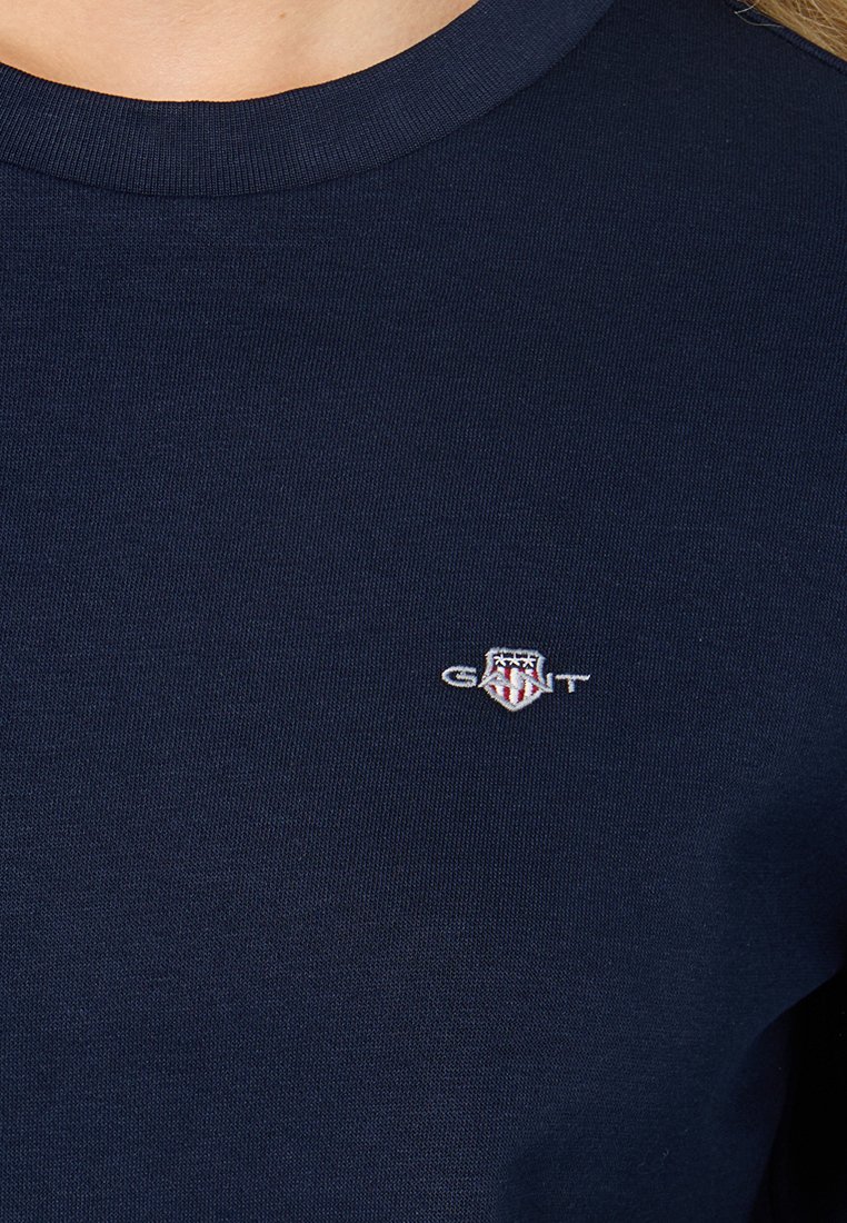Navyblaues Baumwoll-T-Shirt mit Rundhalsausschnitt und einem kleinen gestickten Logo auf der linken Brustseite, ergänzt durch rote und weiße Akzente.