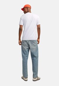 Hvid bomulds T-shirt, afslappet pasform, parret med lyseblå denimjeans. Rød kasket og afslappede sneakers fuldender outfittet.