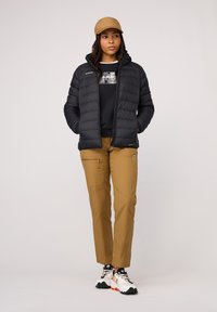 Svart puffjacka med huva, beige keps, svart sweatshirt, khakifärgade byxor och vita sneakers med orange accenter, samt dragkedjsfickor.