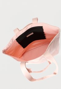 Svetloružová taška na rameno s širokými rukoväťami, otvoreným vrchom a čiernou vreckovou sieťovinou so zipsom vo vnútri na jednoduchom svetlom pozadí.