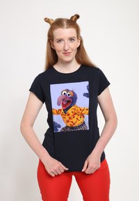 Marinblå t-shirt med en stor tryck av en docka som bär en gul skjorta med röda mönster, i kombination med rutiga shorts.