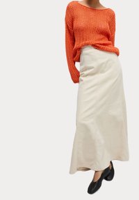 Gehaakt oranje sweatshirt, relaxte pasvorm, lange mouwen, gecombineerd met een crèmekleurige, vloerlange rok met zijnaad en zwarte ballet flats.