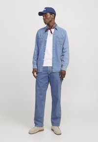 Camisa de mezclilla en azul claro, combinada con una camiseta blanca y pantalones azules. Los accesorios incluyen una gorra azul y un pañuelo rojo alrededor del cuello.