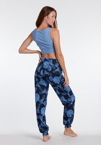 Modrá croptop v kombinácii s tmavo modrými teplákmi so svetlomodrým tropickým vzorom listov; látka vyzerá hladko s elastickými manžetami.